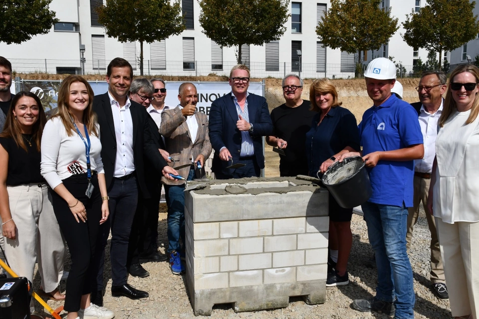 Menschen im Halbkreis um einen Grundstein, die eine Grundsteinlegung feiern Menschen im Halbkreis um einen Grundstein, die eine Grundsteinlegung feiern