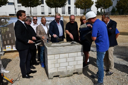 Menschen im Halbkreis um einen Grundstein, die eine Grundsteinlegung vornehmen