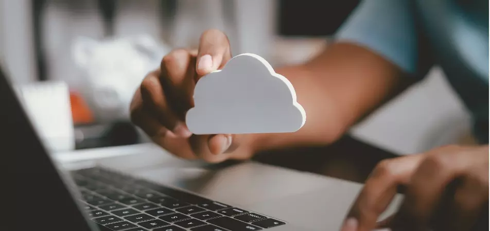 Person arbeitet am Laptop und hält Wolkensymbol hoch Person arbeitet am Laptop und hält Wolkensymbol hoch