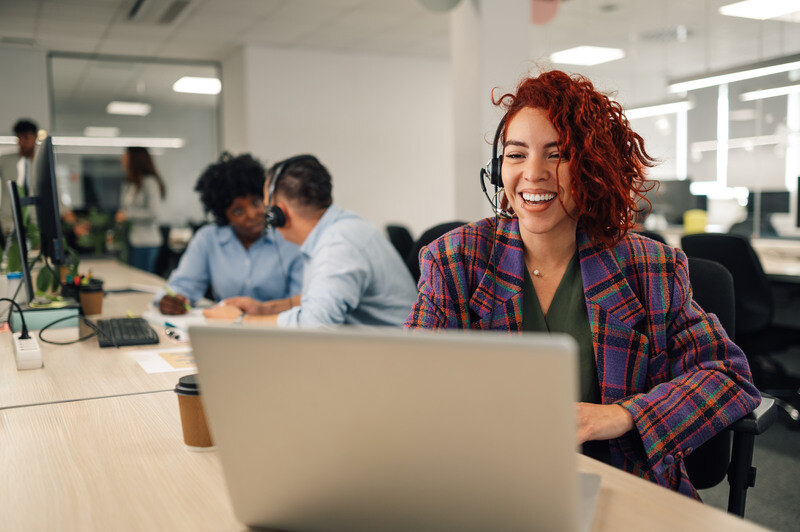 Frau mit Kopfhörern arbeitet im Büro an ihrem Laptop