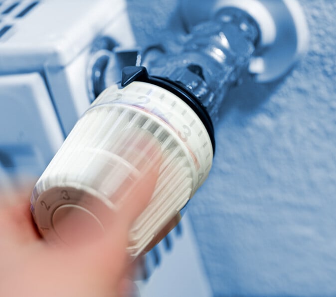 Hand dreht Heizungsregler auf